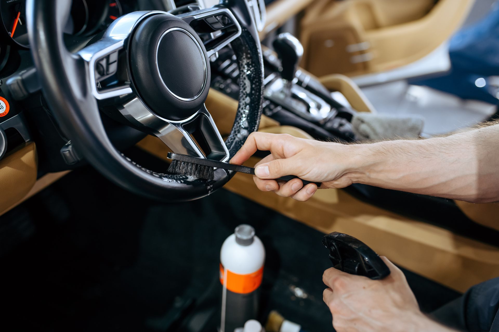 A man is cleaning the steering wheel of a car with a brush.