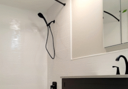 Black showerhead and faucet on a white tiled wall in a bathroom, black cabinet below.