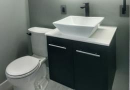 Modern bathroom: white square sink on dark cabinet, toilet next to it.