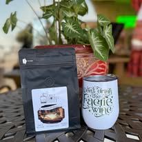 Black coffee bag and white tumbler on a table, plant in background.