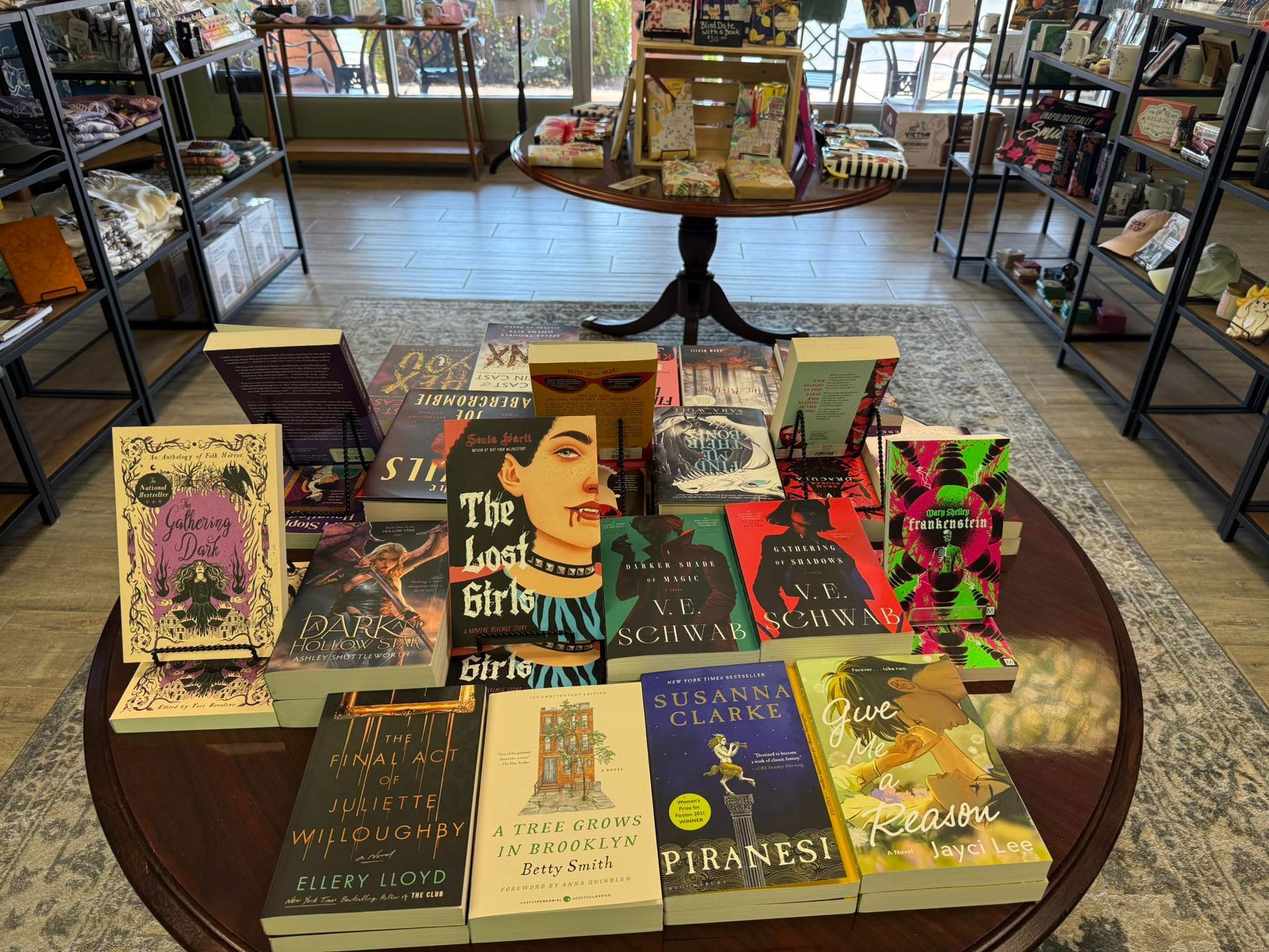 Books displayed on a round table inside a bookstore. Shelves and items are visible in the background.