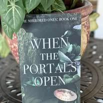 A book titled "When the Portals Open" is in front of a plant pot. The cover is dark with plant imagery.