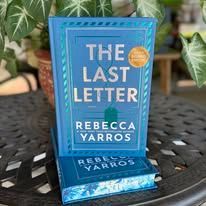Book "The Last Letter" by Rebecca Yarros, blue cover on a table with plants.