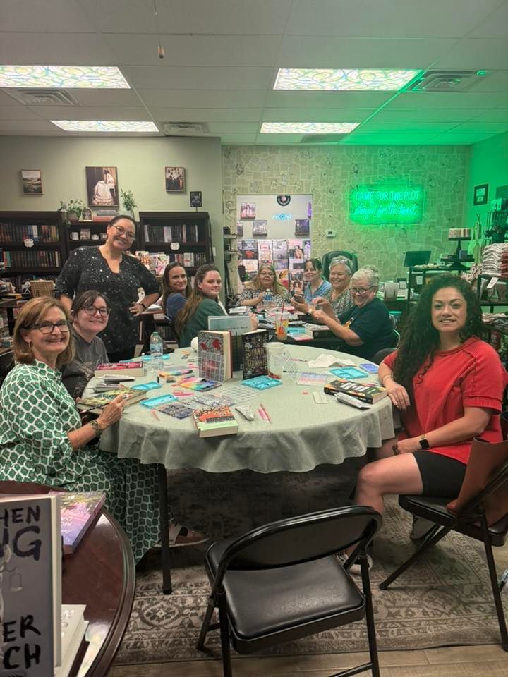 Group of people at a round table, books and papers. Interior setting. Some smiling.