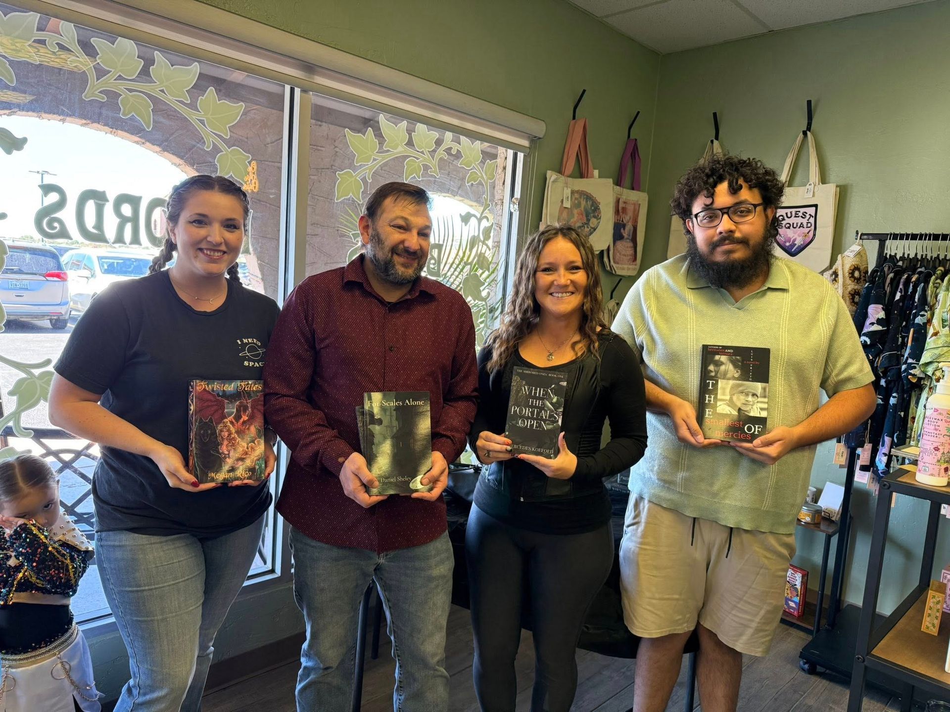 Four people inside a store, each holding a book. Smiling, they stand near a window and clothing rack.