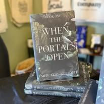 Book cover for "When the Portals Open" stacked with more books on a table.