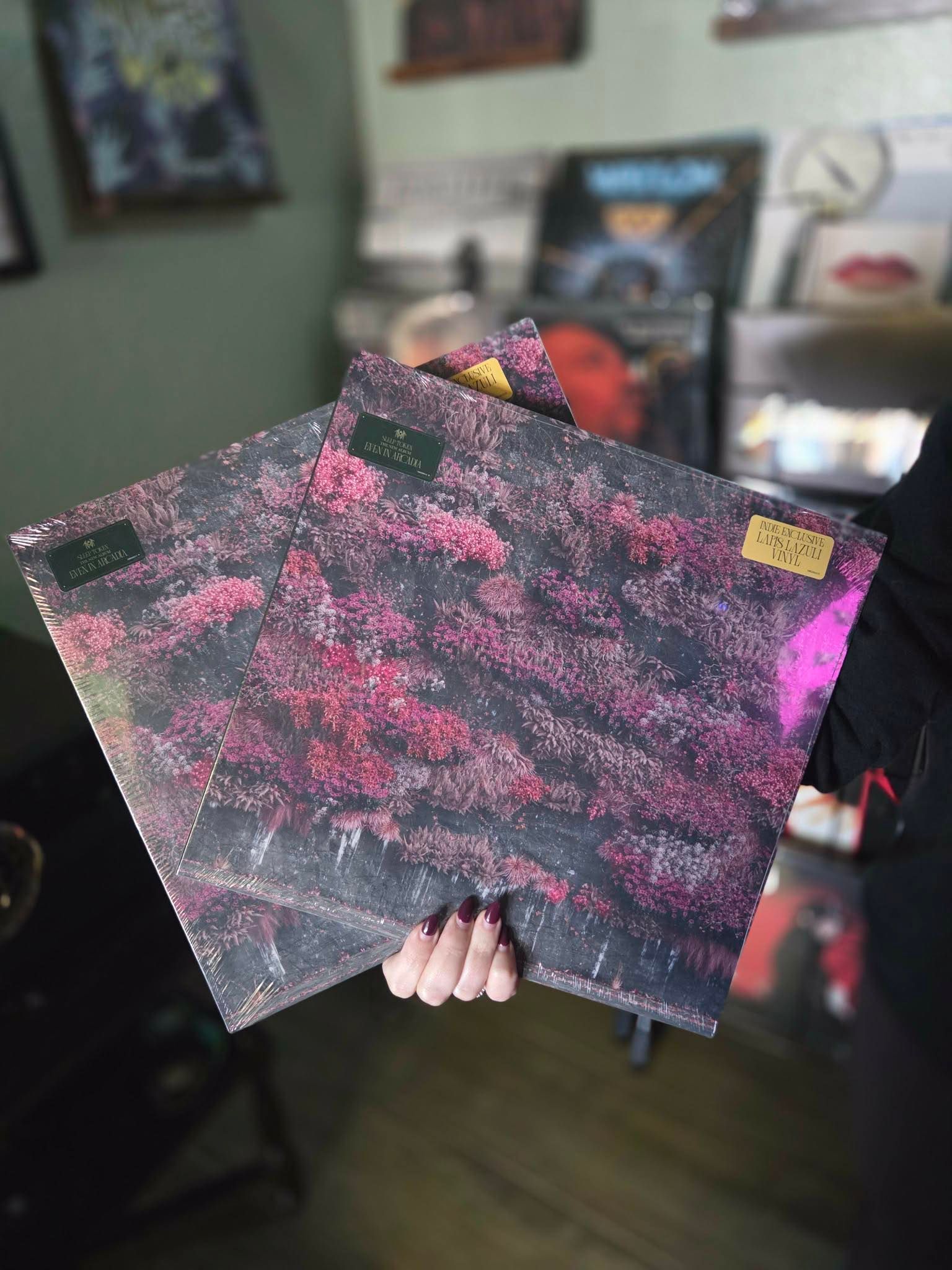 Person holding two vinyl records with pink and black abstract art.