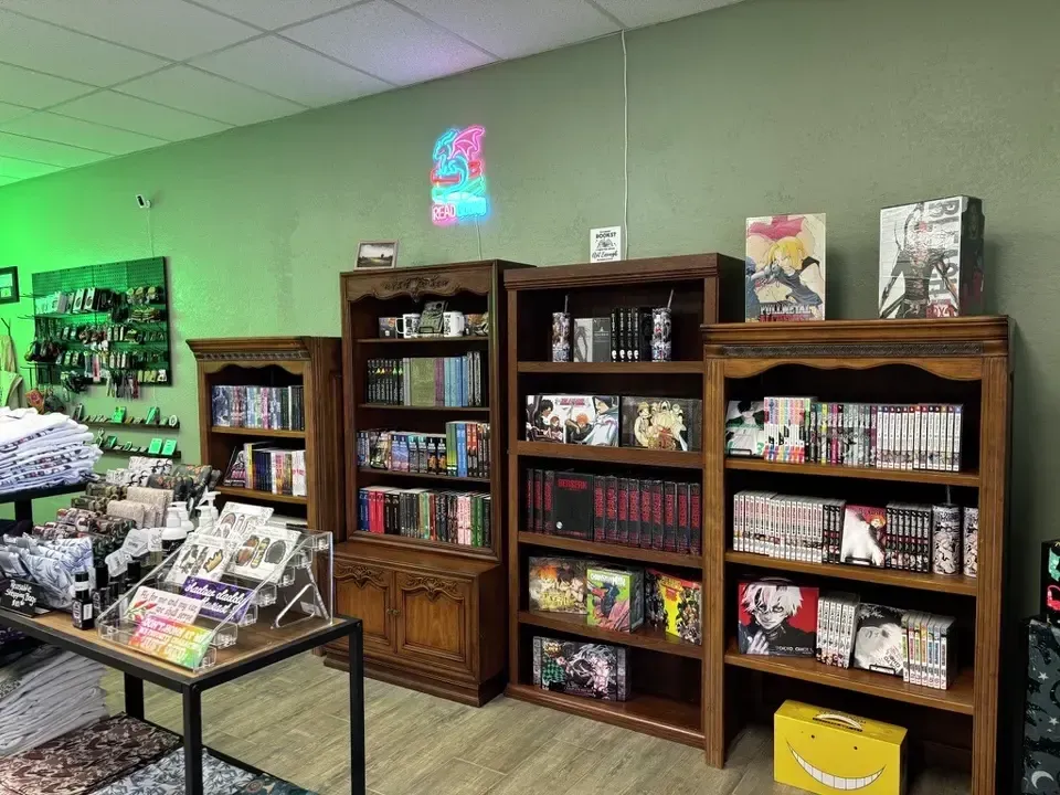 A bookstore interior with wooden shelves filled with manga and books, illuminated by green and colorful lighting.