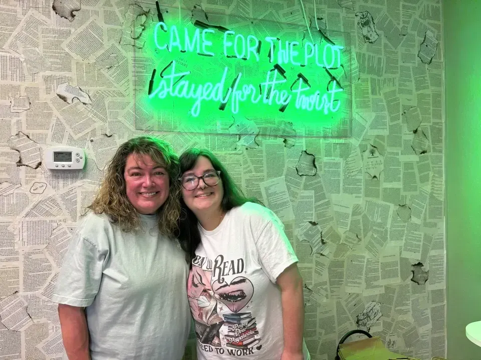 Woman holding small brown bag, smiling at a table with others. Snacks and books in the background.