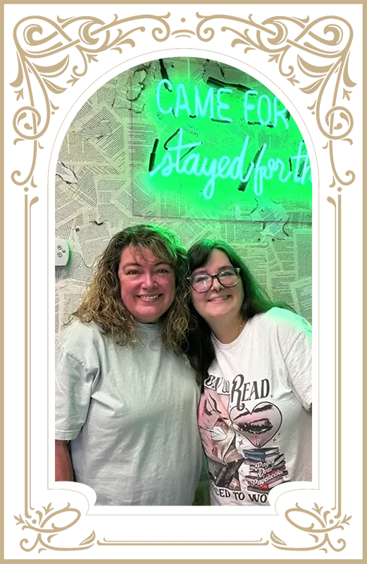 Woman holding small brown bag, smiling at a table with others. Snacks and books in the background.