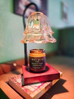 Candle warmer with a jar candle on a stack of books, under a glass lampshade.