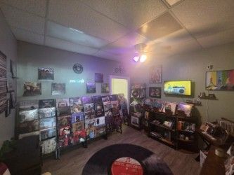 A record store interior with vinyl, art, and a tv. A large record-shaped rug is on the floor.