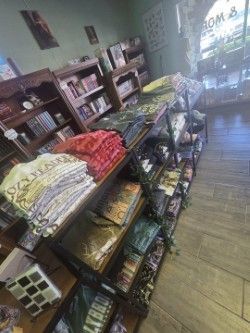 Shelves of merchandise in a store, including t-shirts and books. Wooden shelves, a window, and natural lighting.