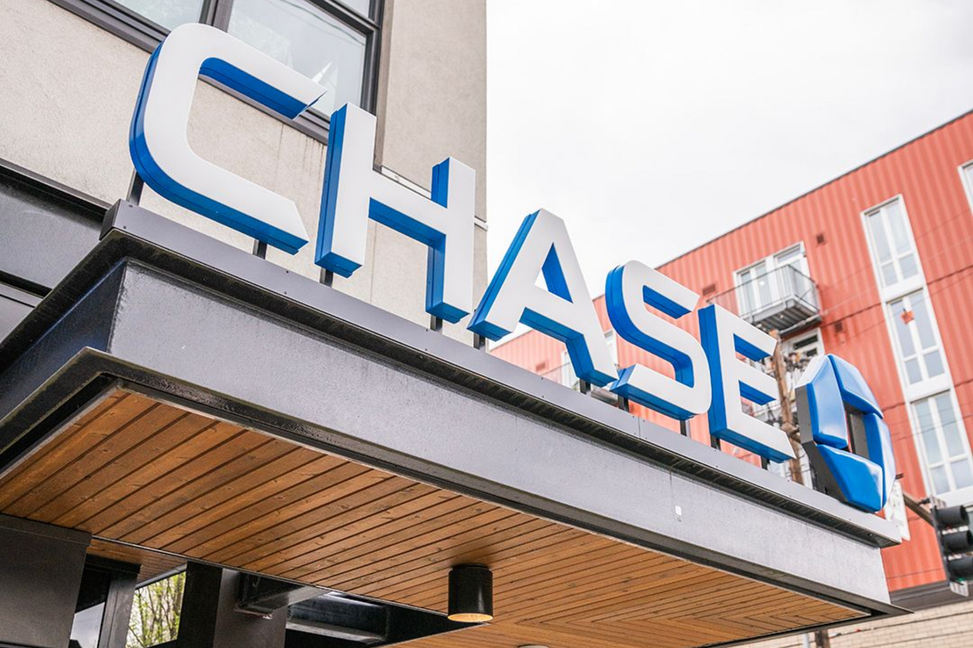 Blue “CHASE” sign on a bank building entrance, viewed from below.