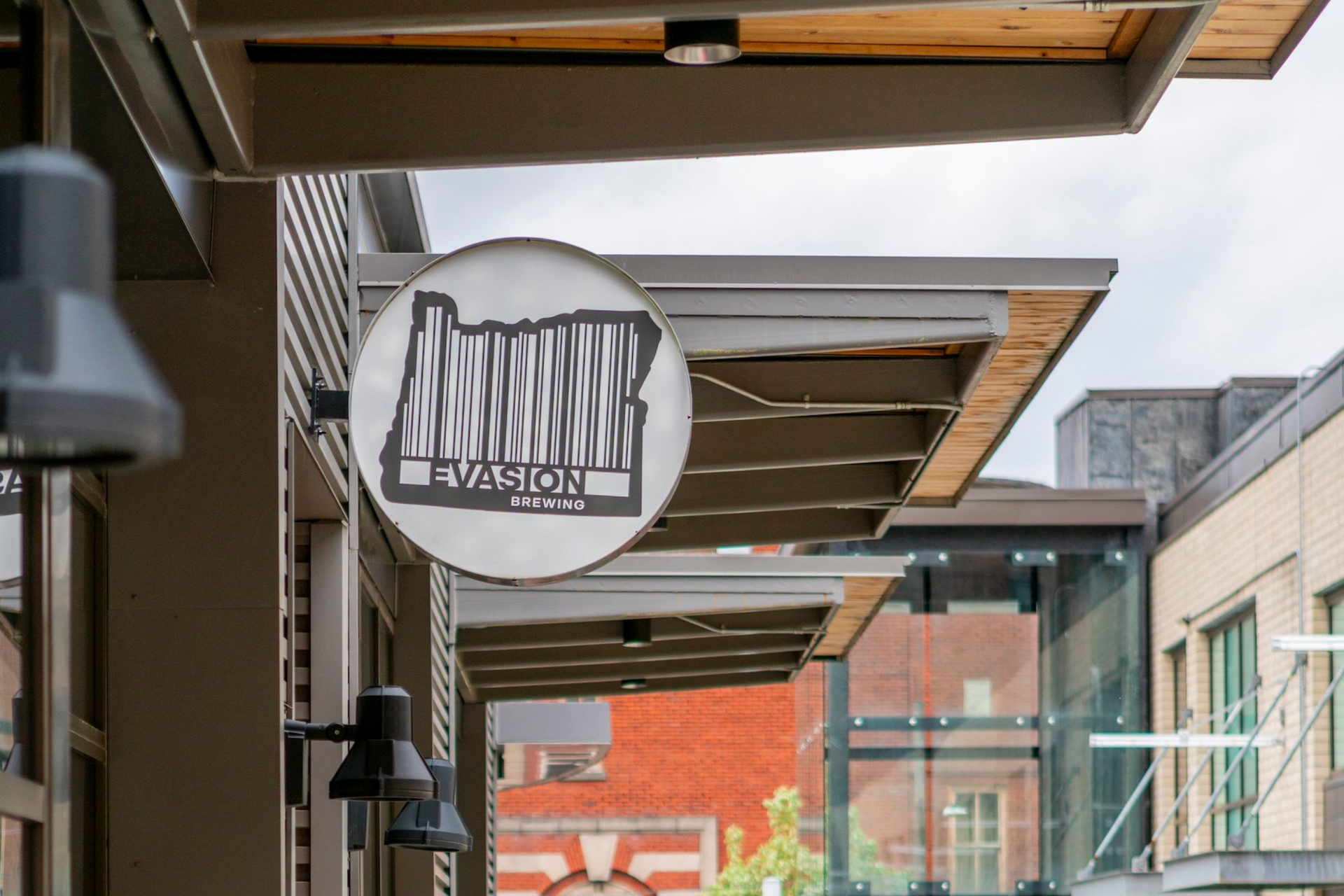 Circular hanging sign on a storefront over a pedestrian walkway, with buildings and glass awnings in the background.
