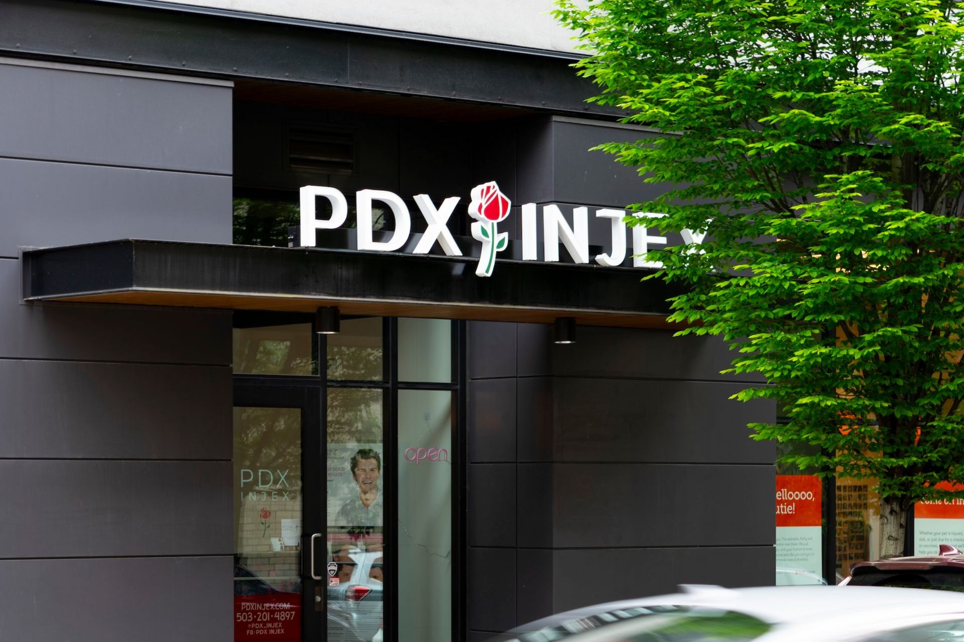 PDX INJE storefront with a passing white car and green tree outside