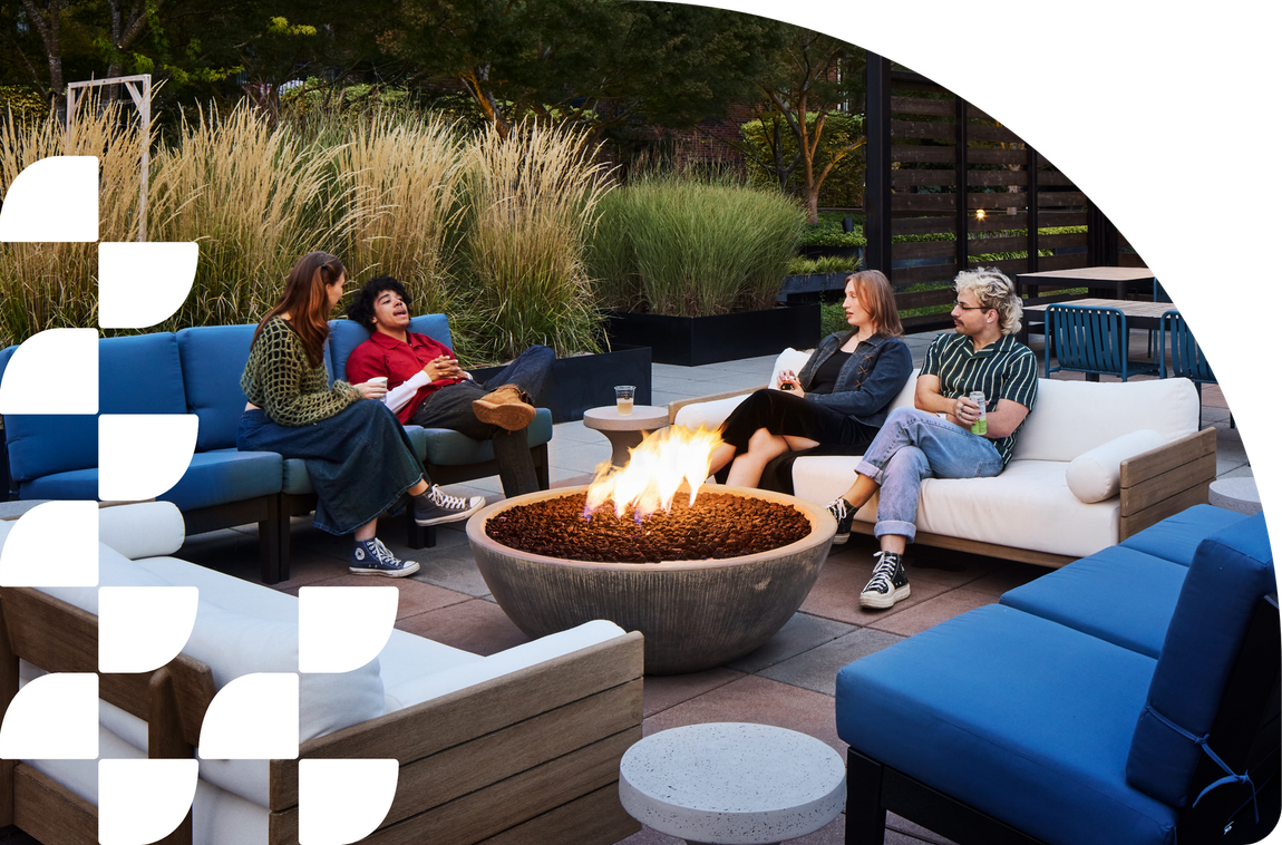 People sitting around a fire pit on a patio with outdoor couches and blue cushions.