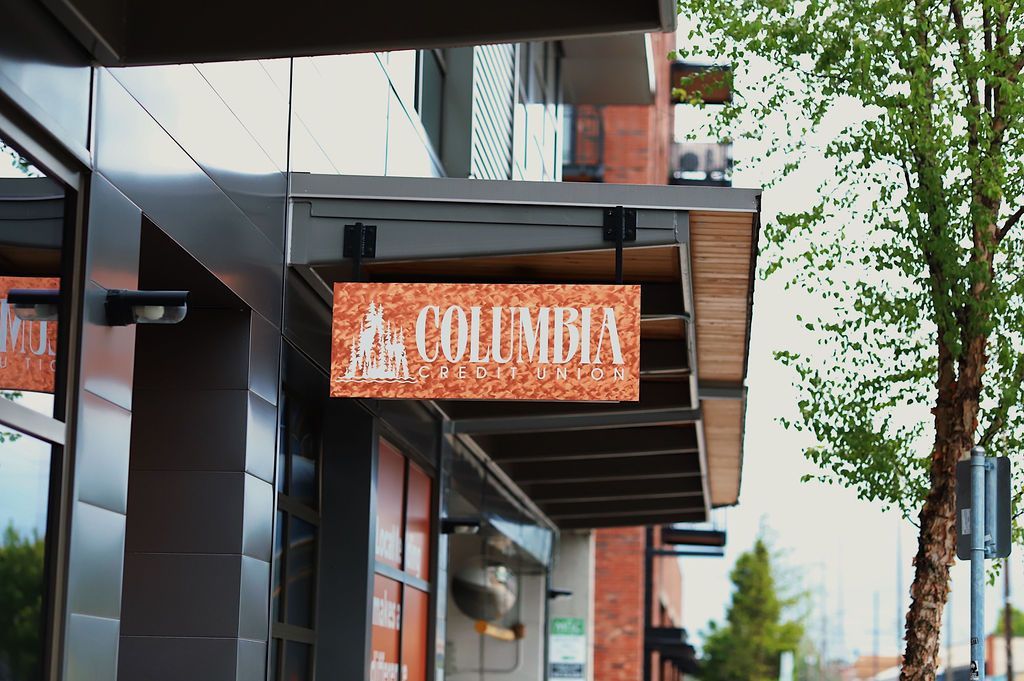 Street view of a storefront with a wooden “COLUMBIA” sign under a black awning