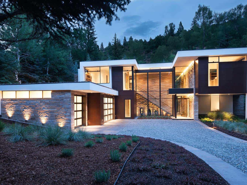 A modern house with a lot of windows is surrounded by trees