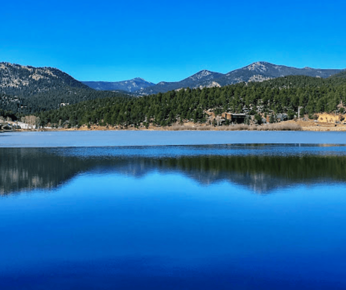 A lake with mountains in the background and trees on the shore.