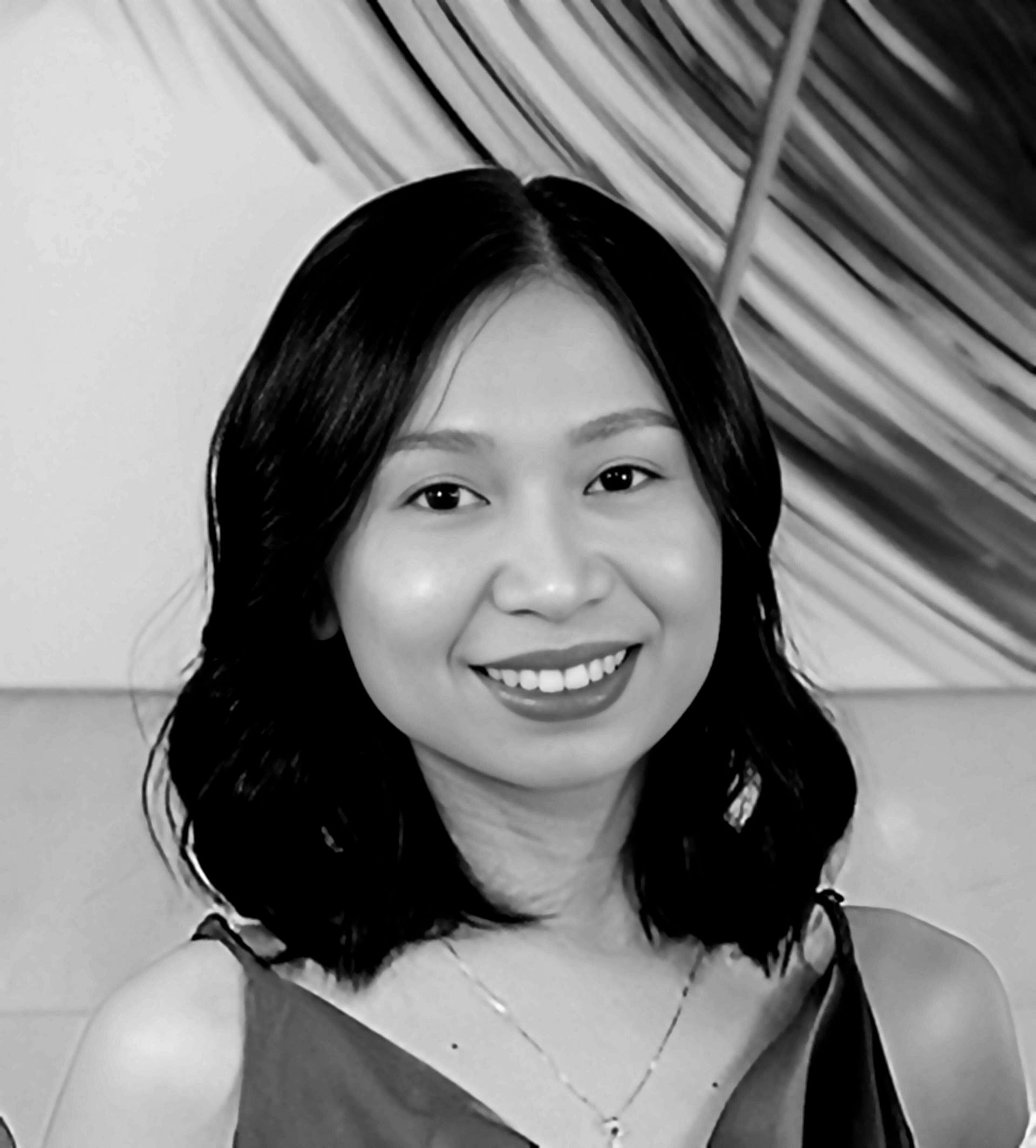 Smiling Asian woman with dark hair, wearing a sleeveless top, in front of a blurred background.