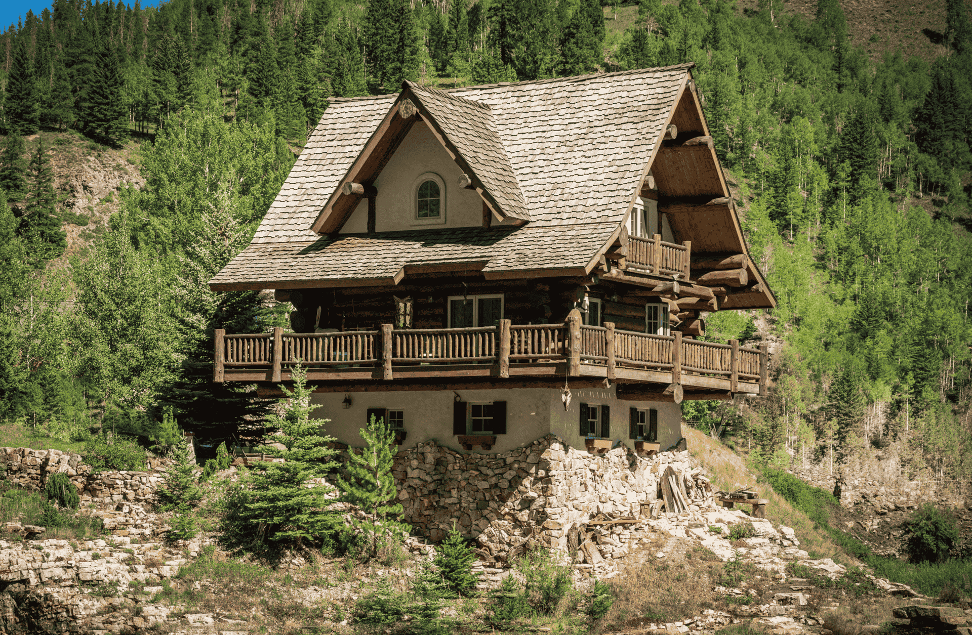 A large log cabin is sitting on top of a rocky hill surrounded by trees.