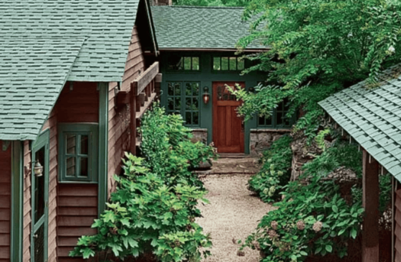 A house with a green roof and a red door is surrounded by trees and bushes.