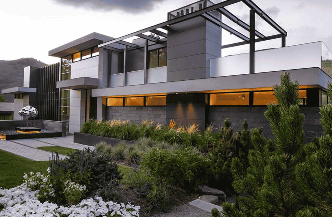 A large modern house with a lot of windows is surrounded by trees and bushes.