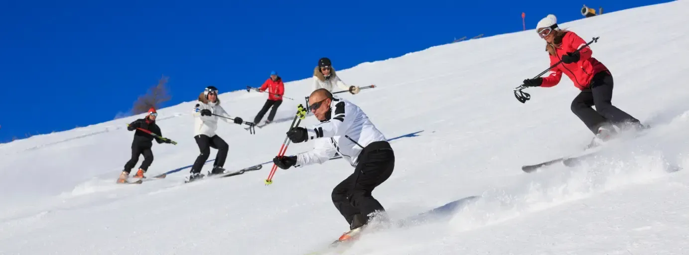 Group of skiers descending a snowy slope under a clear blue sky, with one skier carving a turn in th