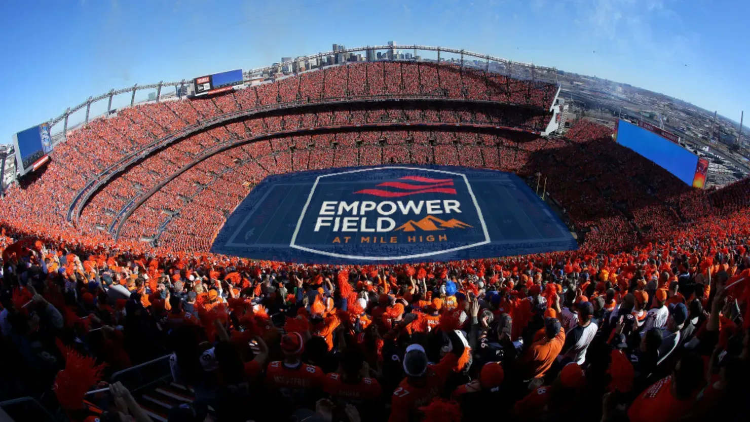 Packed stadium with a large field banner at Empower Field at Mile High.