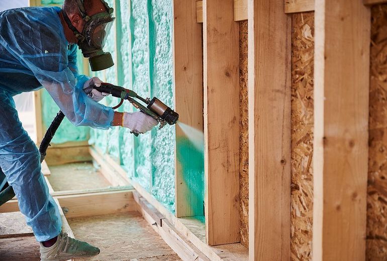 A man is spraying insulation on a wooden wall.