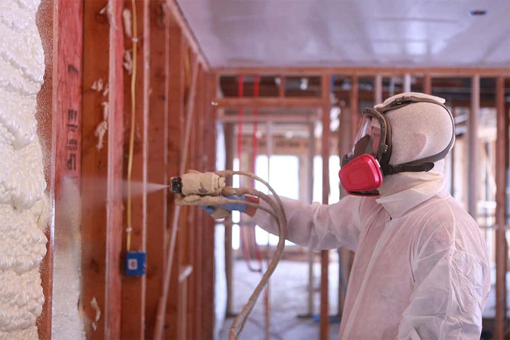 A man is spraying foam on a wall in a building under construction.