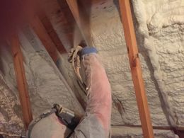 A man is spraying foam on the ceiling of a house.