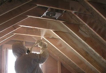 A man is spraying foam on the ceiling of an attic