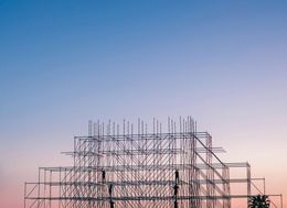 A large building is being built with scaffolding against a sunset sky.
