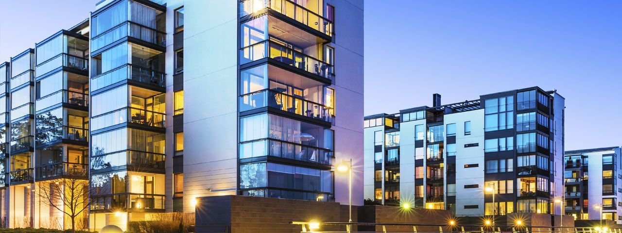 A group of tall buildings with lots of windows are lit up at night.