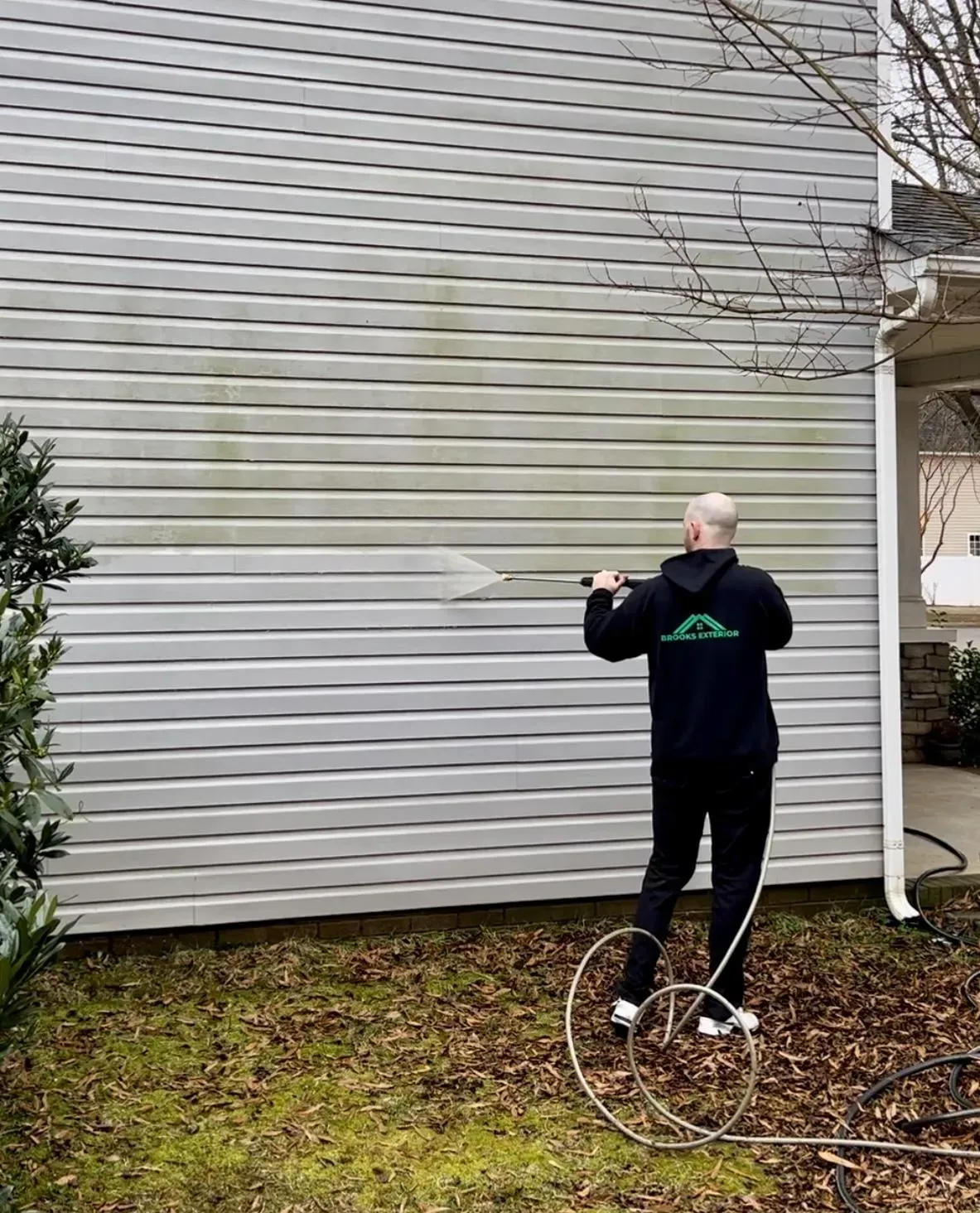 A man is cleaning the side of a house with a pressure washer.