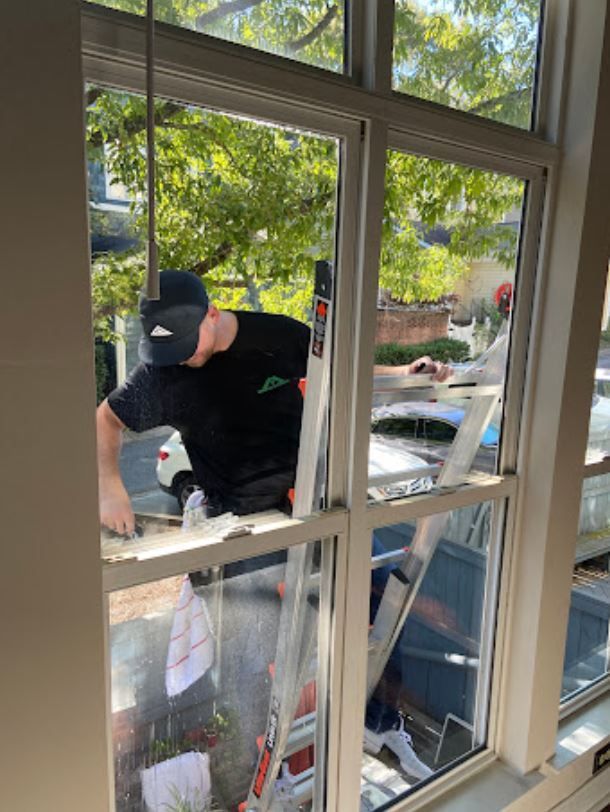 A man is standing on a ladder cleaning a window.