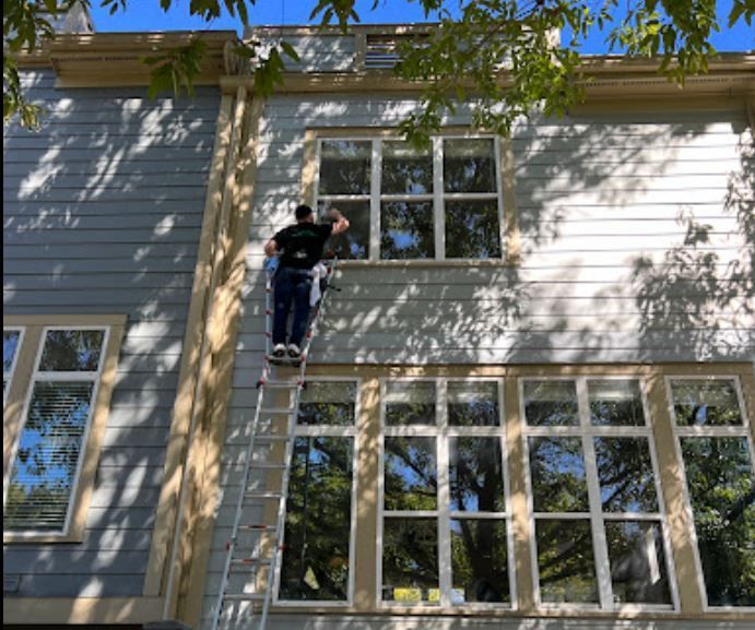 A man is standing on a ladder cleaning a window on the side of a building.