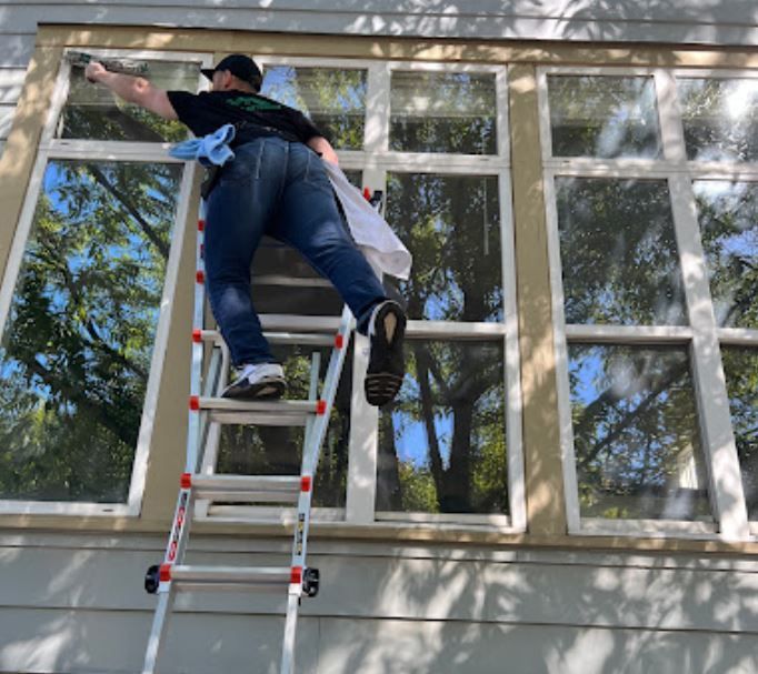 A man is standing on a ladder cleaning a window.
