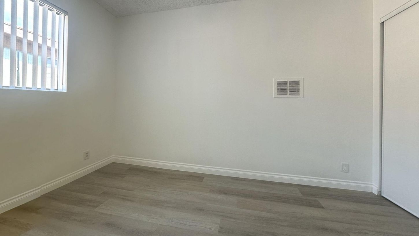 Empty room with a window, white walls, and wood-look flooring.
