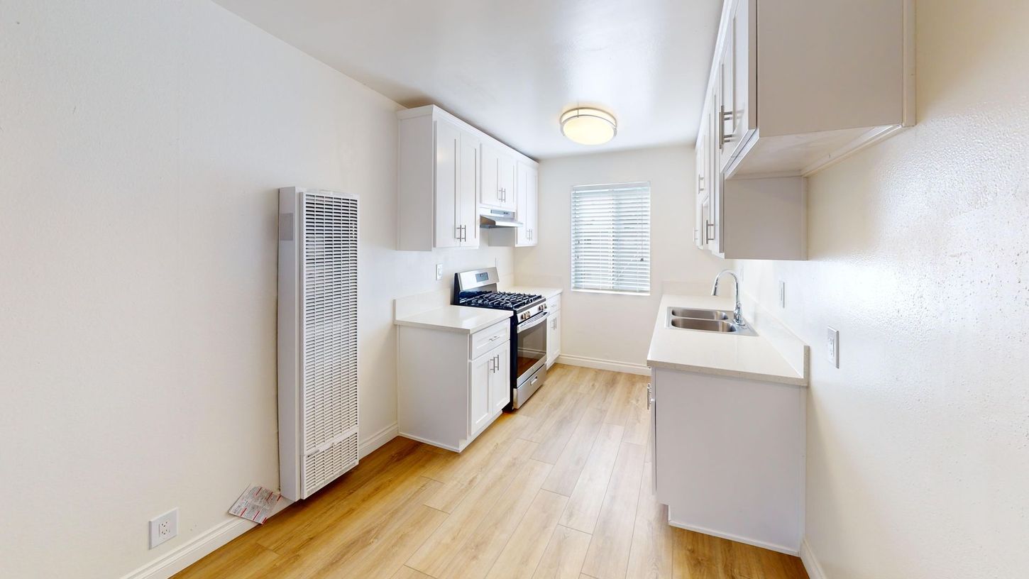 White kitchen with light wood floor, cabinets, appliances, and a radiator.