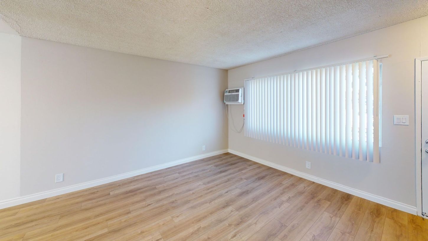 Empty room with light wood floor, beige walls, a window with blinds, and an air conditioning unit.