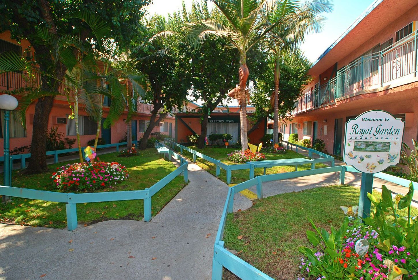 Courtyard of a pink apartment complex with a turquoise fence, greenery, and sign.