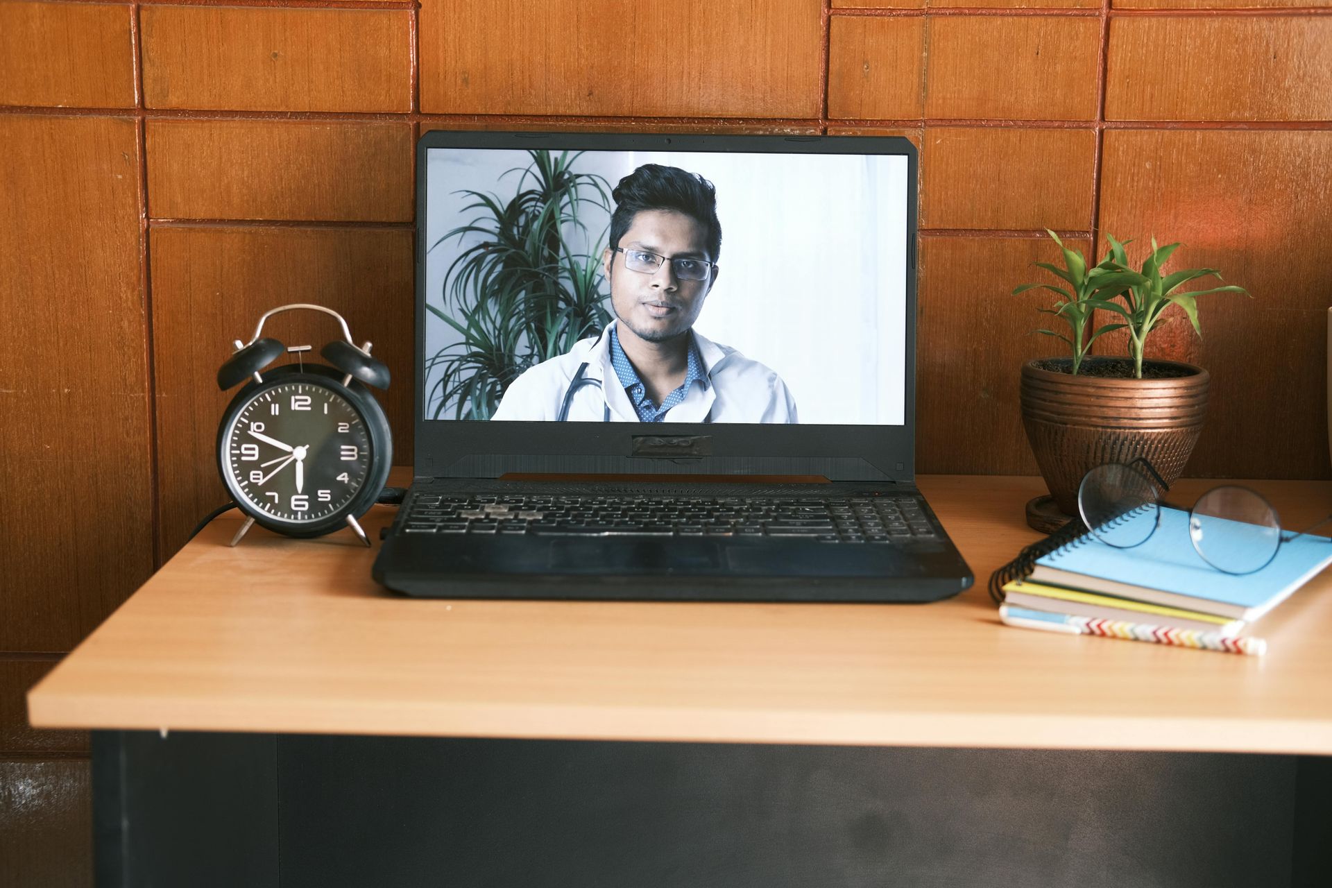 A laptop computer is sitting on a wooden desk next to an alarm clock.