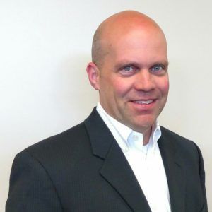 A bald man in a suit and white shirt smiles for the camera