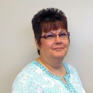 A woman wearing glasses and a blue shirt is smiling for the camera.