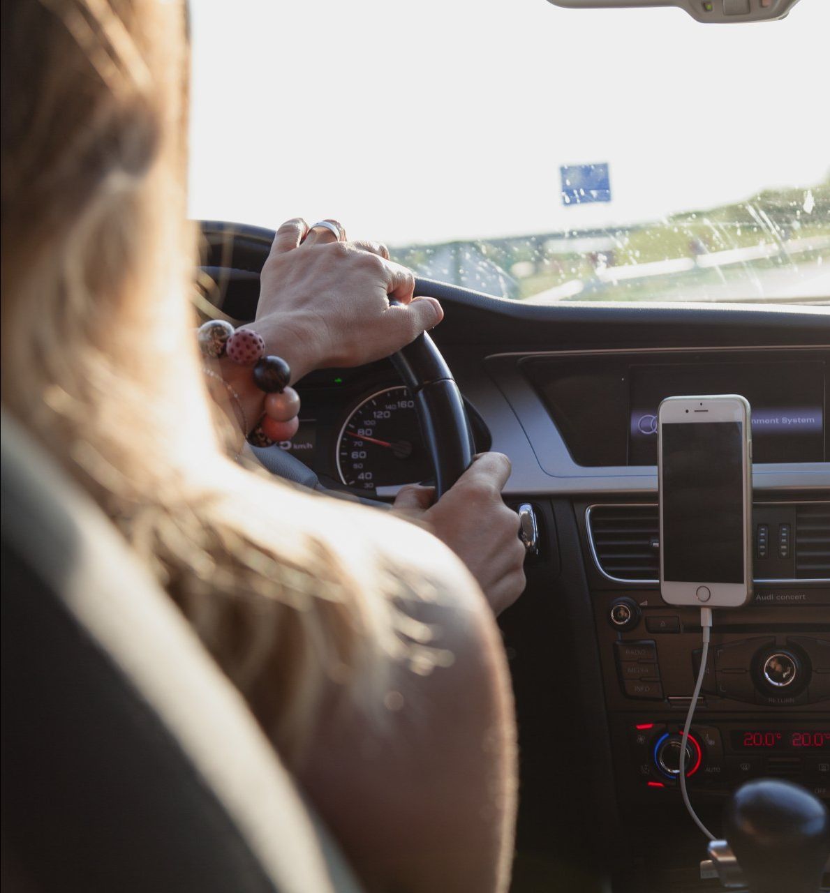 A woman is driving a car with a cell phone plugged into the dashboard.