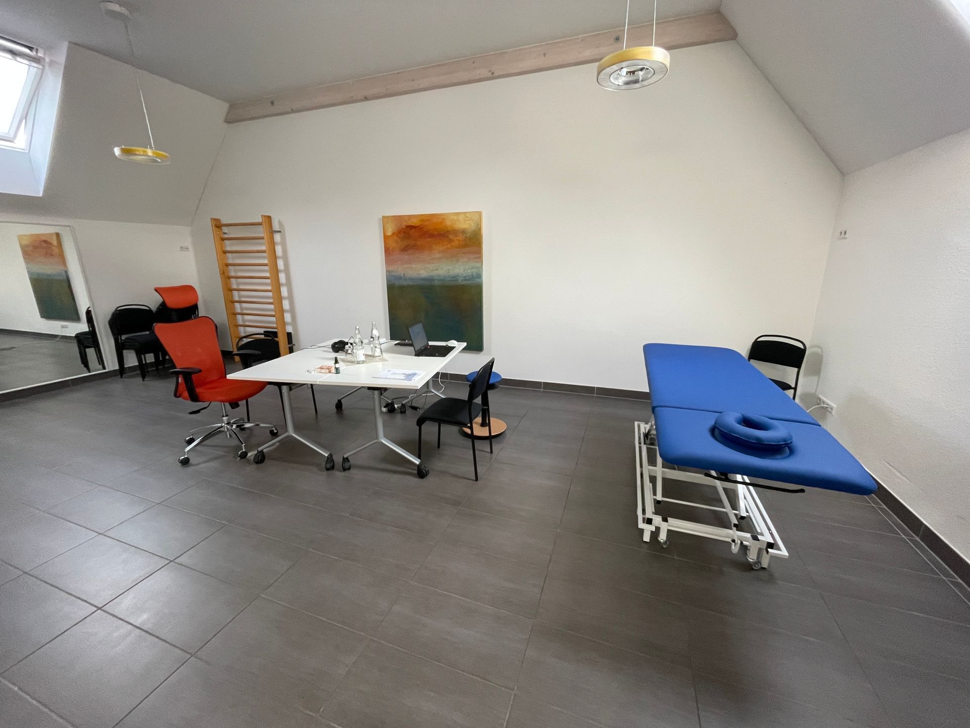 Ein Behandlungszimmer mit einem Tisch, Stühlen und einer blauen Liege.
