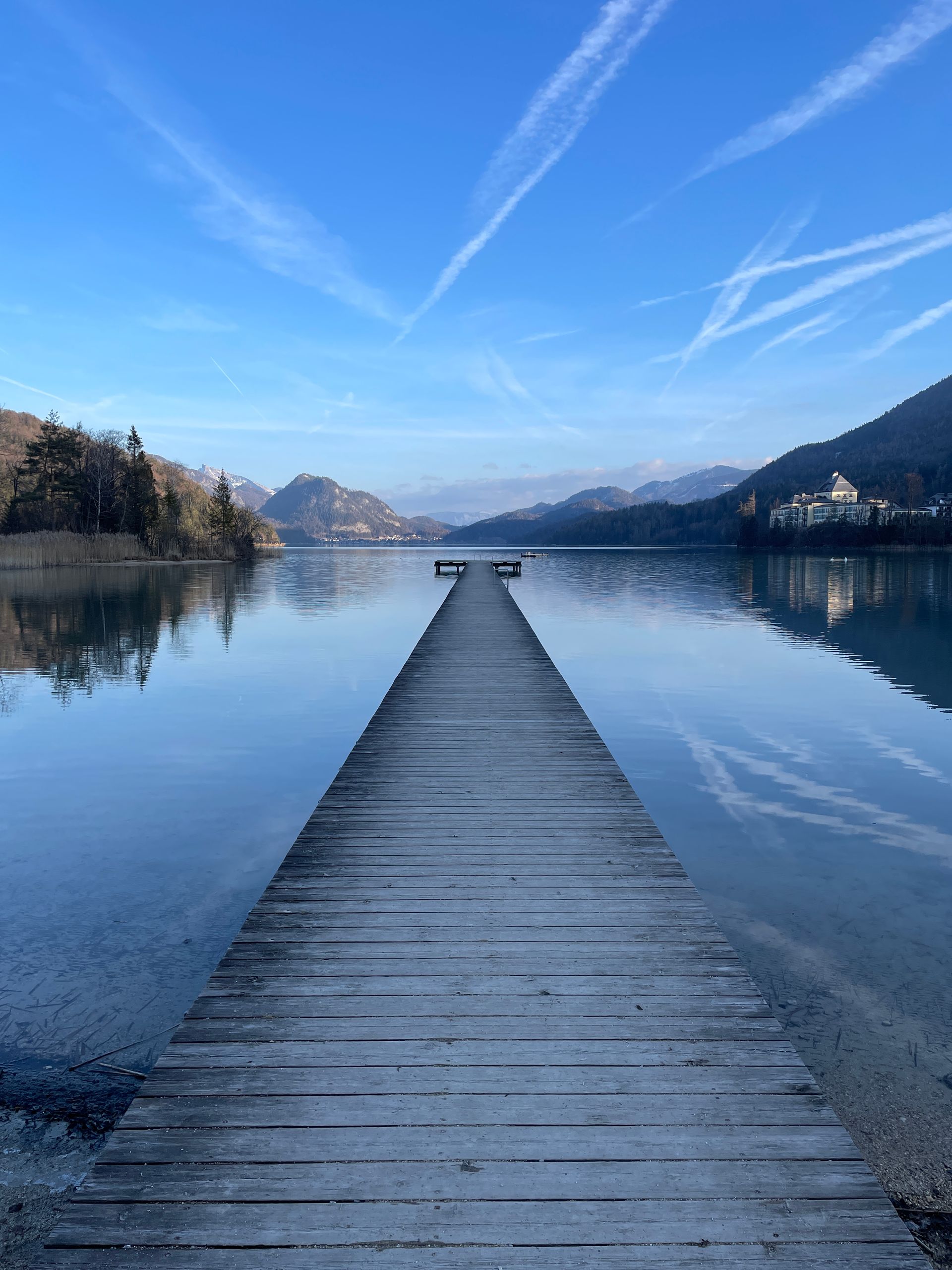 Ein Holzsteg, der zu einem See mit Bergen im Hintergrund führt.